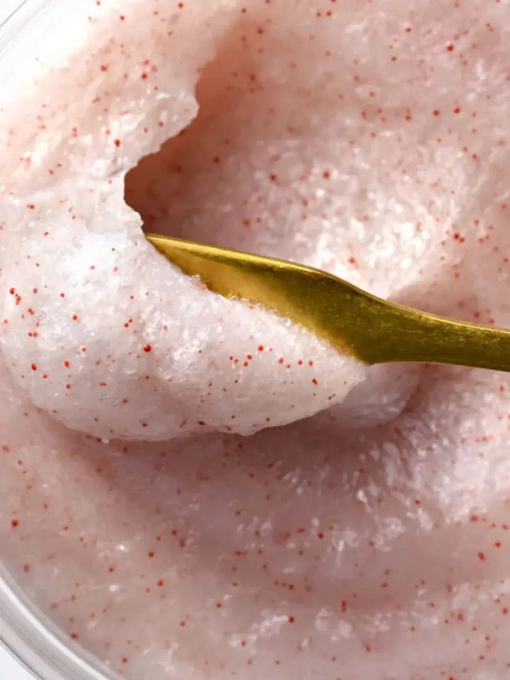 A close-up shot shows a gold spoon scooping a portion of the textured, pinkish-white Davines SOLU Sea Salt Scrub Cleanser speckled with red exfoliating beads | Twentyseven Toronto