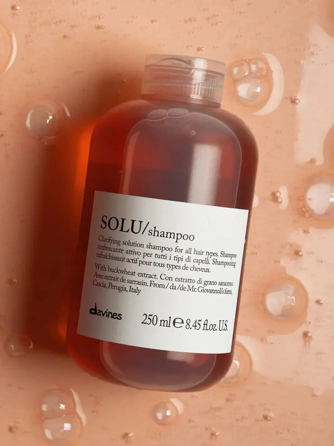 A bottle of Davines SOLU Shampoo is immersed in a glossy, amber-colored gel or liquid filled with scattered air bubbles | Twentyseven Toronto
