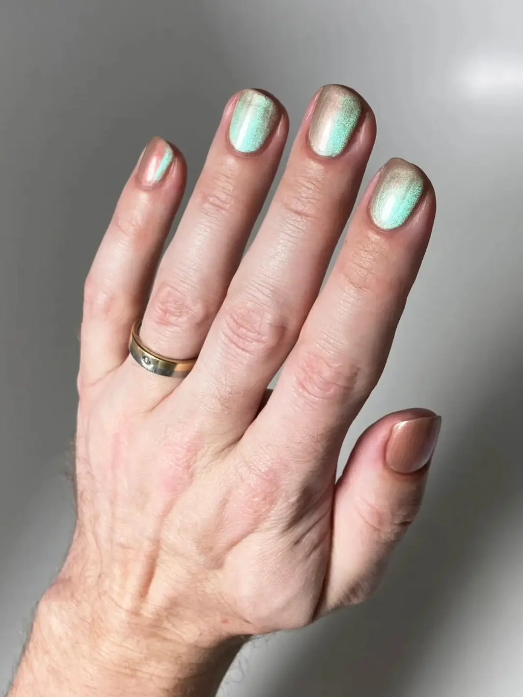 Hand with glittery pink and light green gradient nails using 'Something Else' magnetic nail polish by Death Valley Nails wearing a ring on a neutral background | Twentyseven Toronto