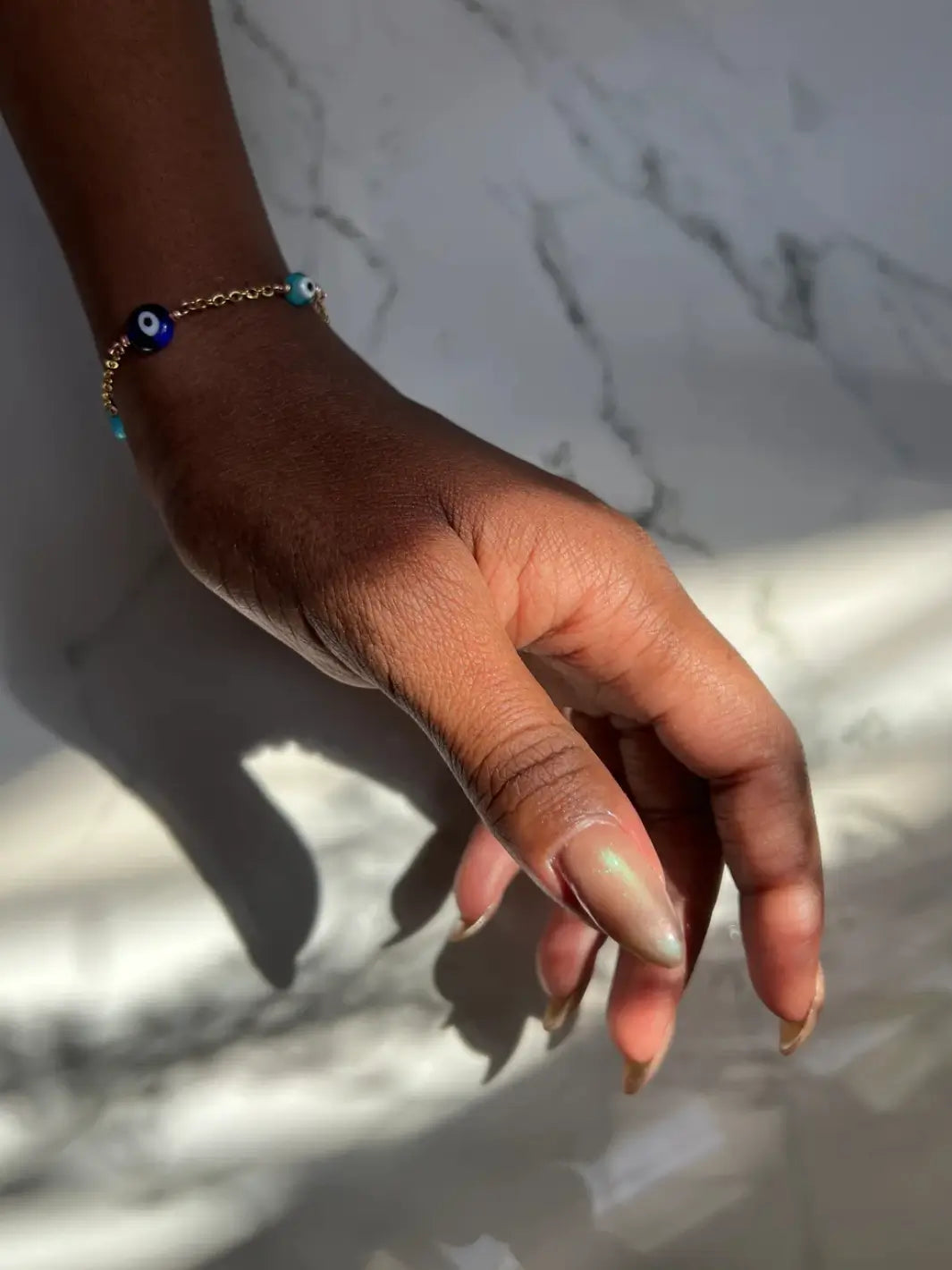 Hand with long pink and light green gradient nails using 'Something Else' magnetic nail polish by Death Valley Nails wearing a bracelet on a marble background | Twentyseven Toronto
