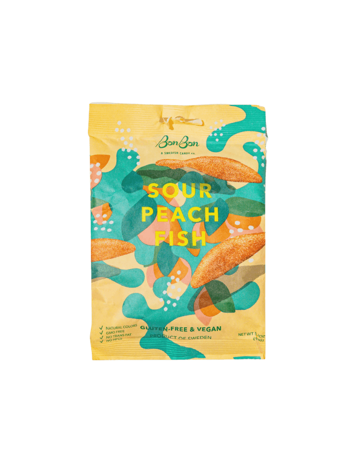 A sealed yellow pouch featuring abstract green, teal, and peach graphics displays the front packaging of Sour Peach Fish Swedish Candy from BonBon NYC against a transparent background | Twentyseven Toronto