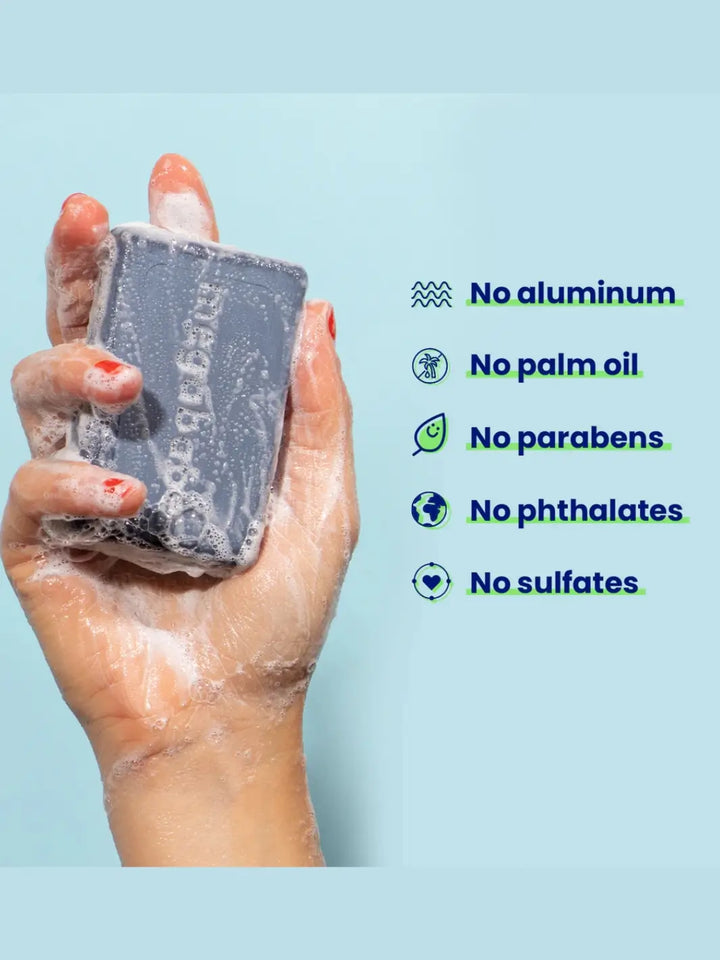 Hand holding a bar soap 'Space Bar' from Megababe with a list of ingredients on a light blue background | Twentyseven Toronto