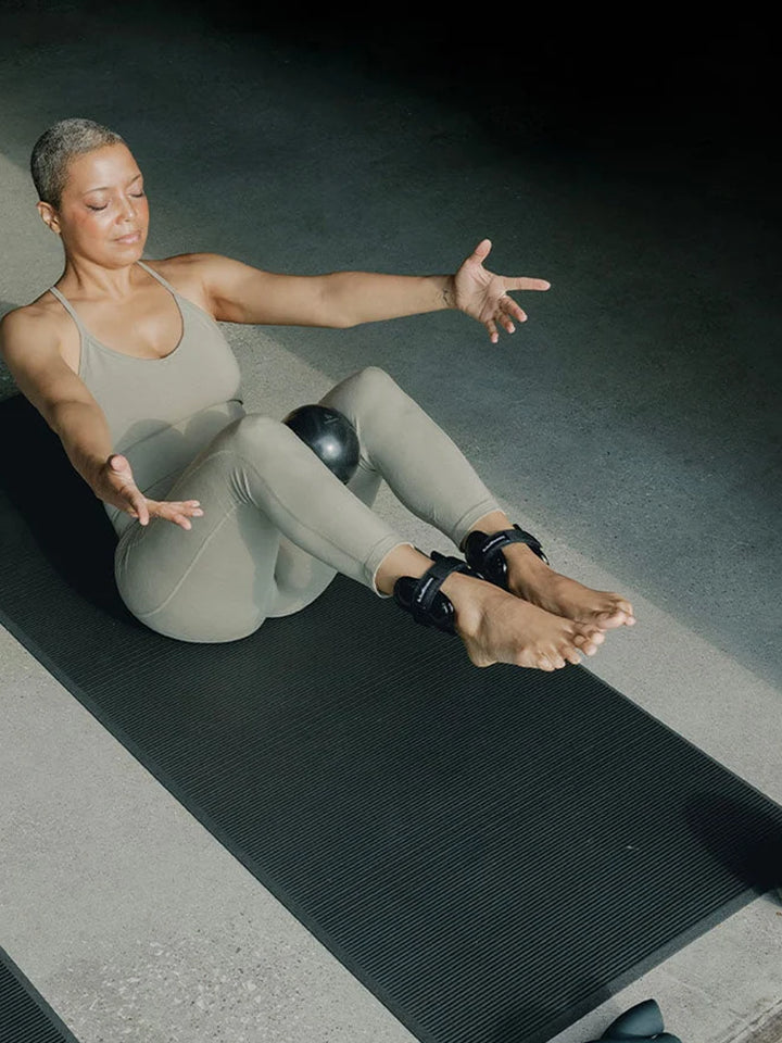 Person using a black Halfmoon Sphere Weight for stability work on an exercise mat | Twentyseven Toronto