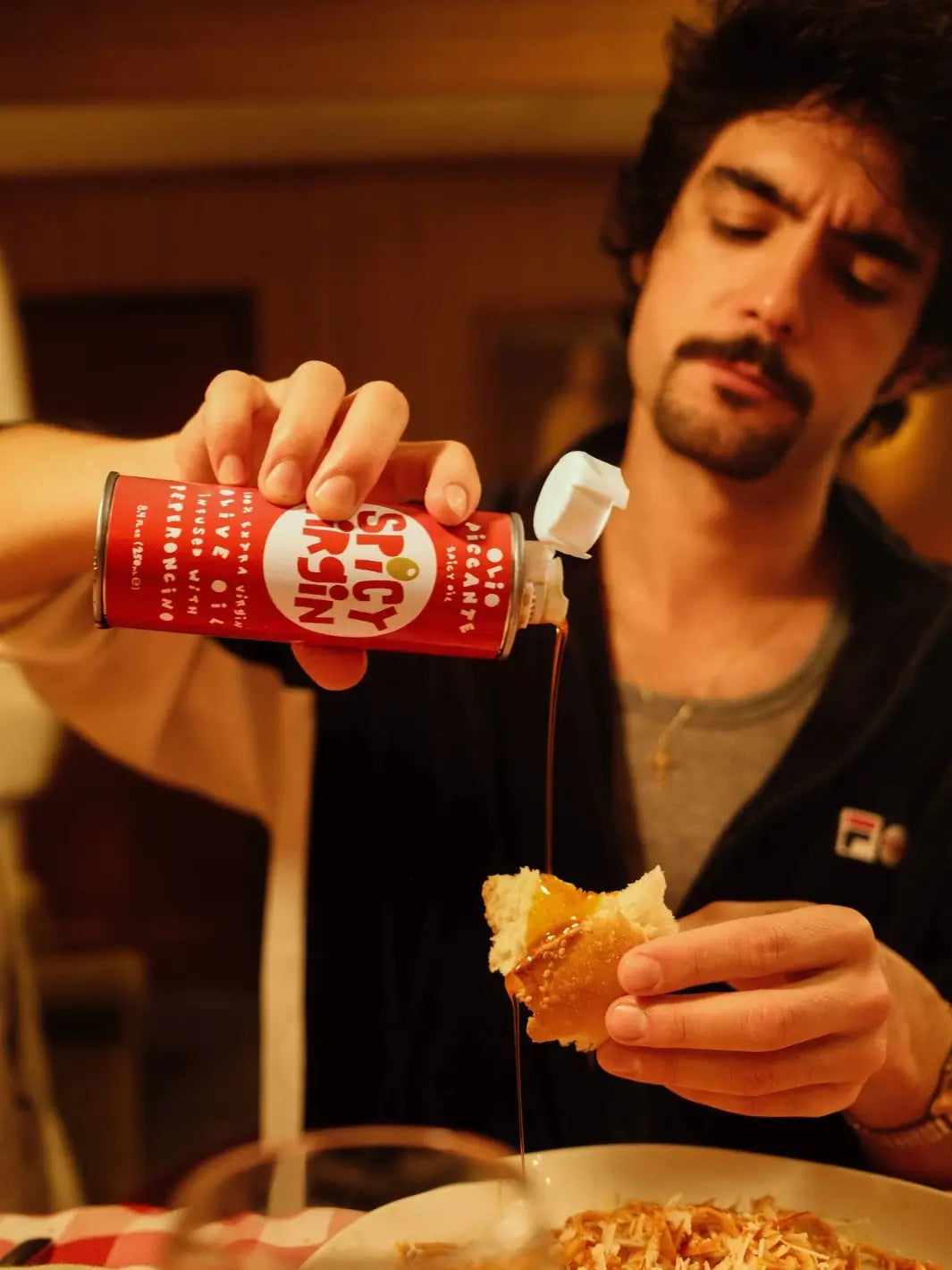 Person pouring Casa Virgin Spicy Virgin Olive Oil from a can onto a piece of bread | Twentyseven Toronto