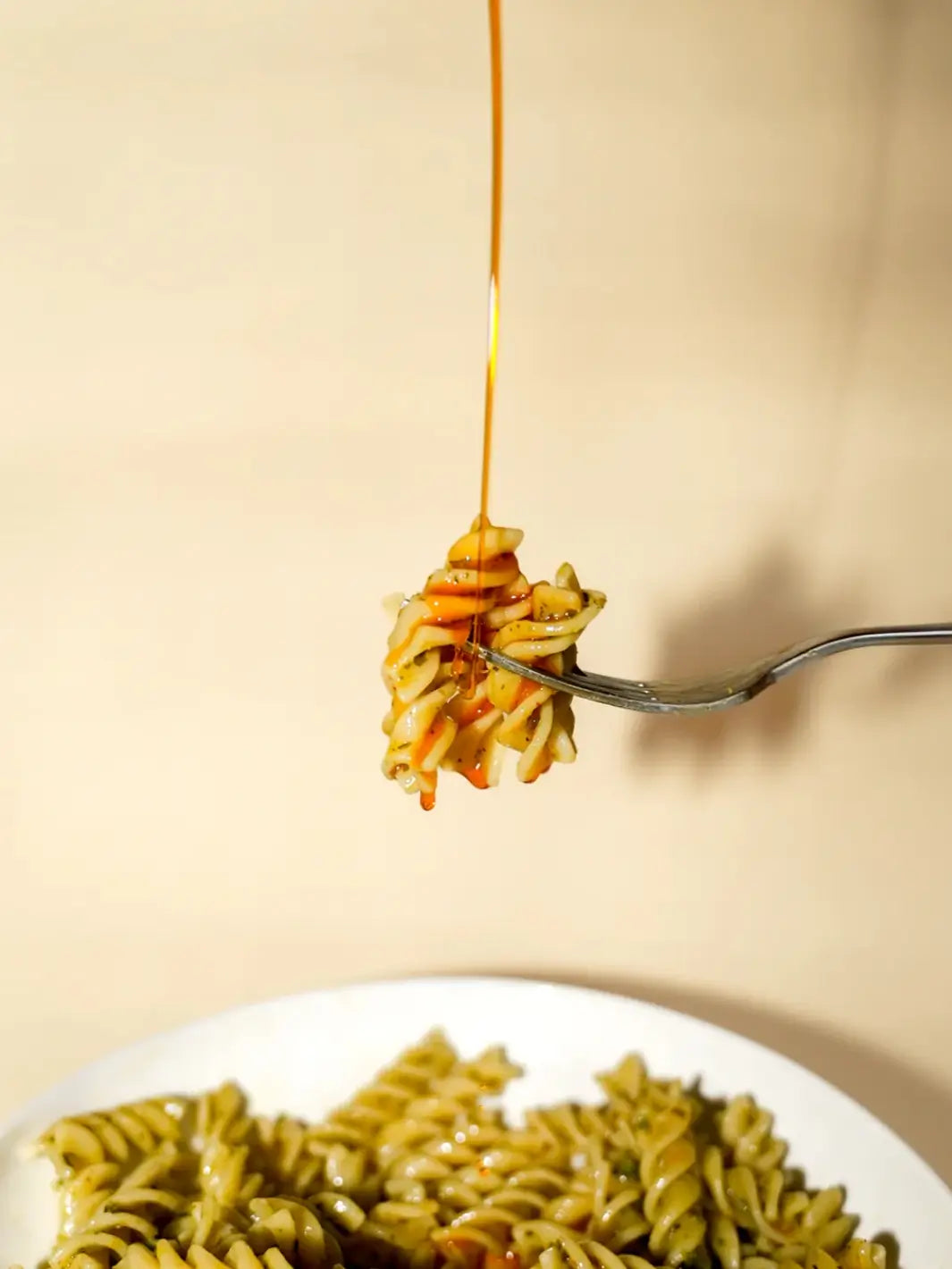 Spicy Virgin Olive Oil from Casa Virgin dripping on pasta on a fork against a beige background | Twentyseven Toronto