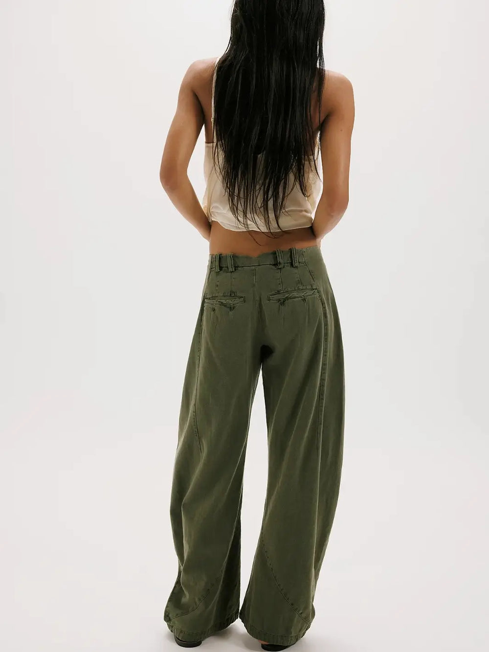 A rear view of a model showcasing the back pocket detailing, belt loops, and relaxed wide-leg fit of the dark green Free People Spotlight Washed Barrel Chino Trousers in Dusty Olive | Twentyseven Toronto