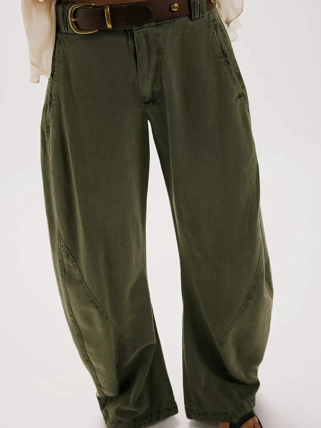 A front mid-section shot focusing on the curved seams, side pockets, and a dark leather belt styled with the dark green Free People Spotlight Washed Barrel Chino Trousers in Dusty Olive | Twentyseven Toronto