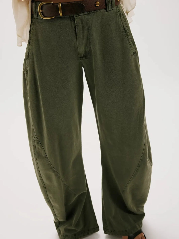 A front mid-section shot focusing on the curved seams, side pockets, and a dark leather belt styled with the dark green Free People Spotlight Washed Barrel Chino Trousers in Dusty Olive | Twentyseven Toronto