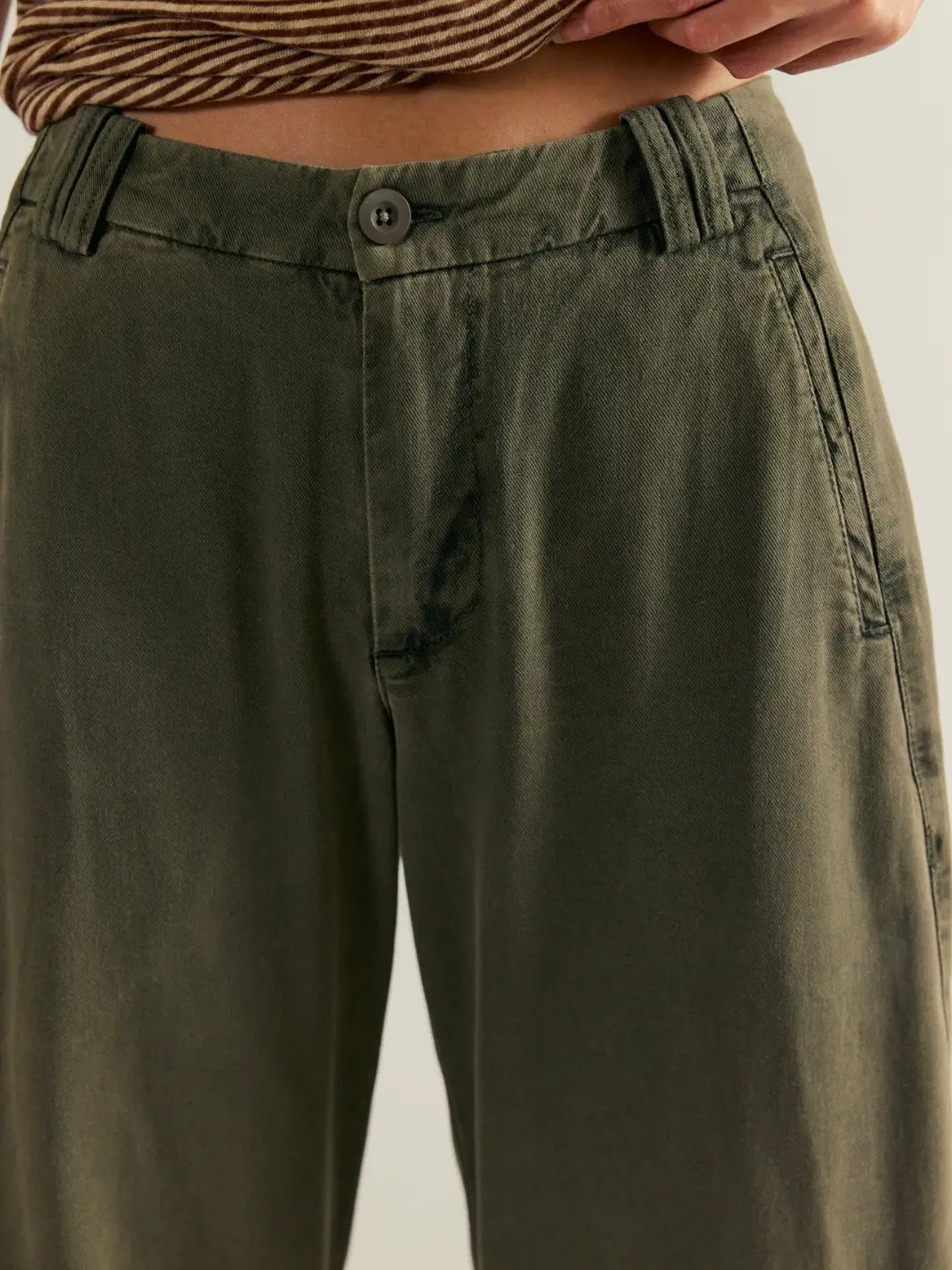 A close-up detail shot highlighting the front button closure, zipper fly, and washed textured fabric of the dark green Free People Spotlight Washed Barrel Chino Trousers in Dusty Olive | Twentyseven Toronto