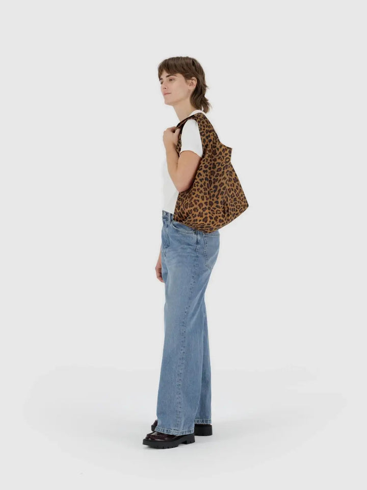 A lifestyle shot shows a person carrying the BAGGU Standard Baggu in Leopard over their shoulder against a white background | Twentyseven Toronto