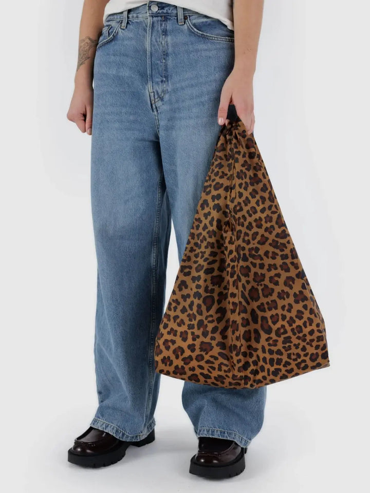A person wearing wide-leg jeans and lug-sole loafers holds a BAGGU Standard Baggu in Leopard against a white background | Twentyseven Toronto