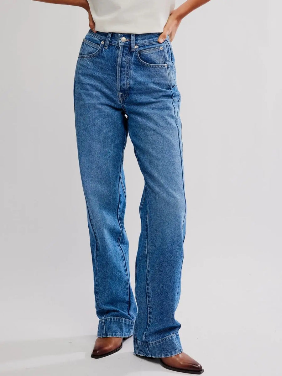 A front view shows a model wearing the high-waisted, medium-wash Free People Stick Around Slim Curve Jeans - Stay For The Morning with brown pointed boots | Twentyseven Toronto