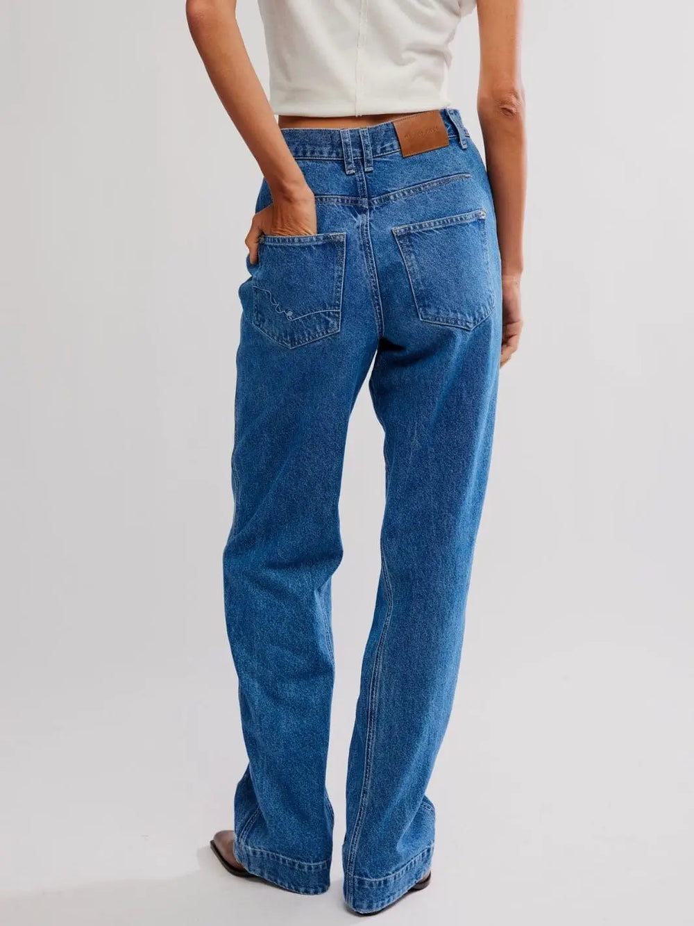 A rear view features a model with their hand in the back pocket, showing the leather brand patch on the Free People Stick Around Slim Curve Jeans - Stay For The Morning | Twentyseven Toronto