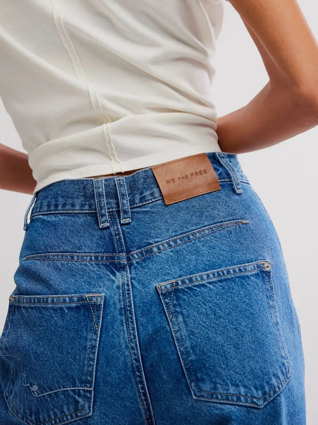 A close-up back shot focuses on the "We The Free" leather label, back pockets, and denim texture of the Free People Stick Around Slim Curve Jeans - Stay For The Morning | Twentyseven Toronto