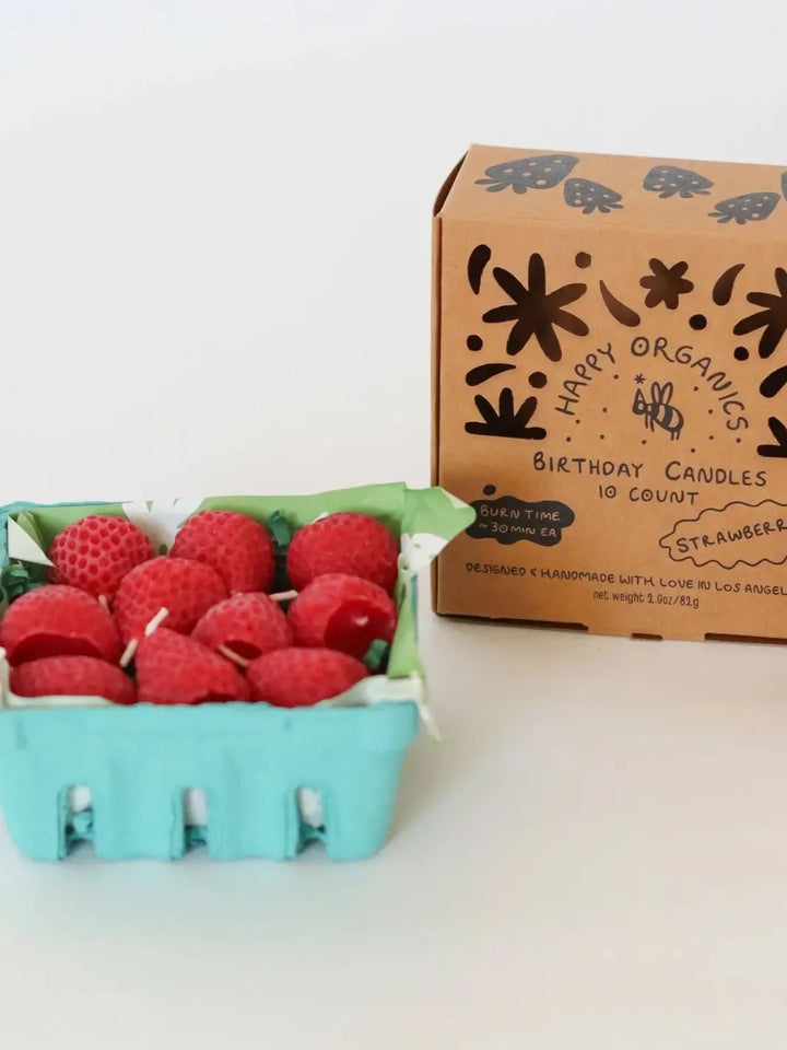 Carton of red birthday candles shaped like strawberries next to a box labeled 'Happy Organics' on a light background | Twentyseven Toronto