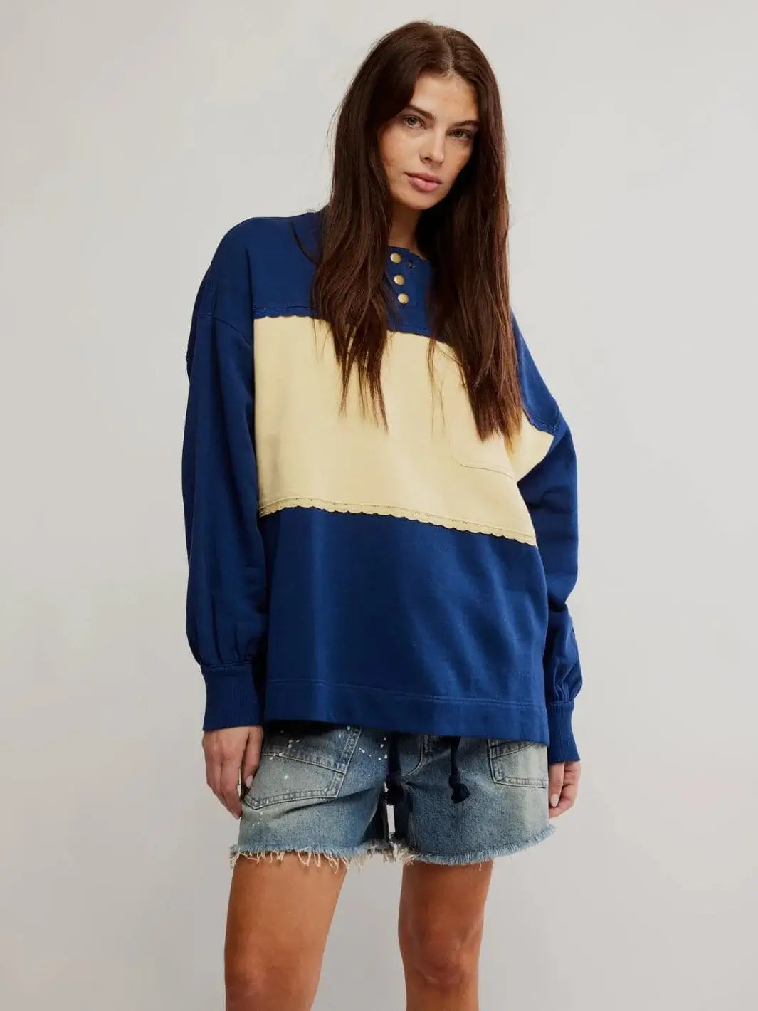 A front view shows a model posing in the oversized Free People Strawberry Sweatshirt - Oceana Combo with a three-button neckline and distressed denim shorts | Twentyseven Toronto