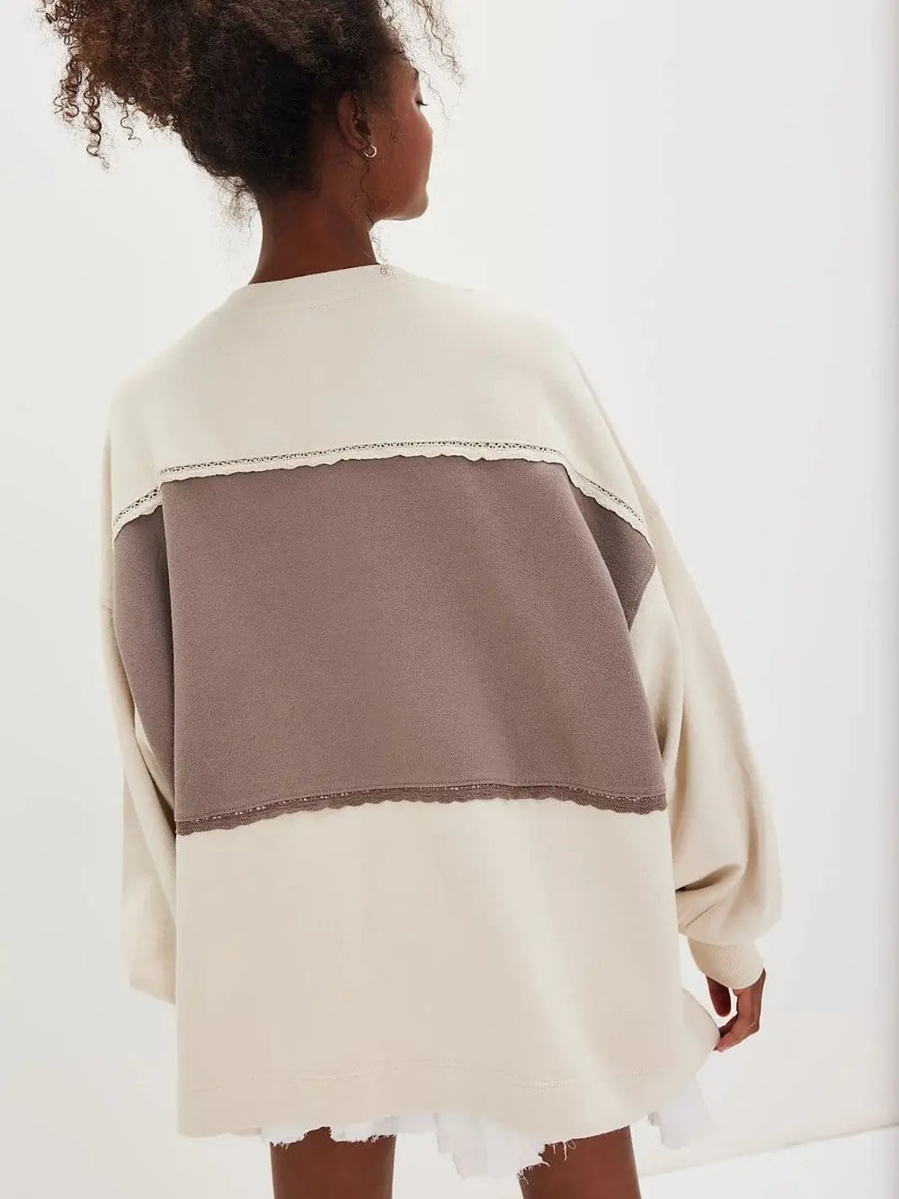 Rear view of a model highlighting the large, light brown color-blocked panel on the back of the Free People Strawberry Sweatshirt - Summer Sand Combo | Twentyseven Toronto