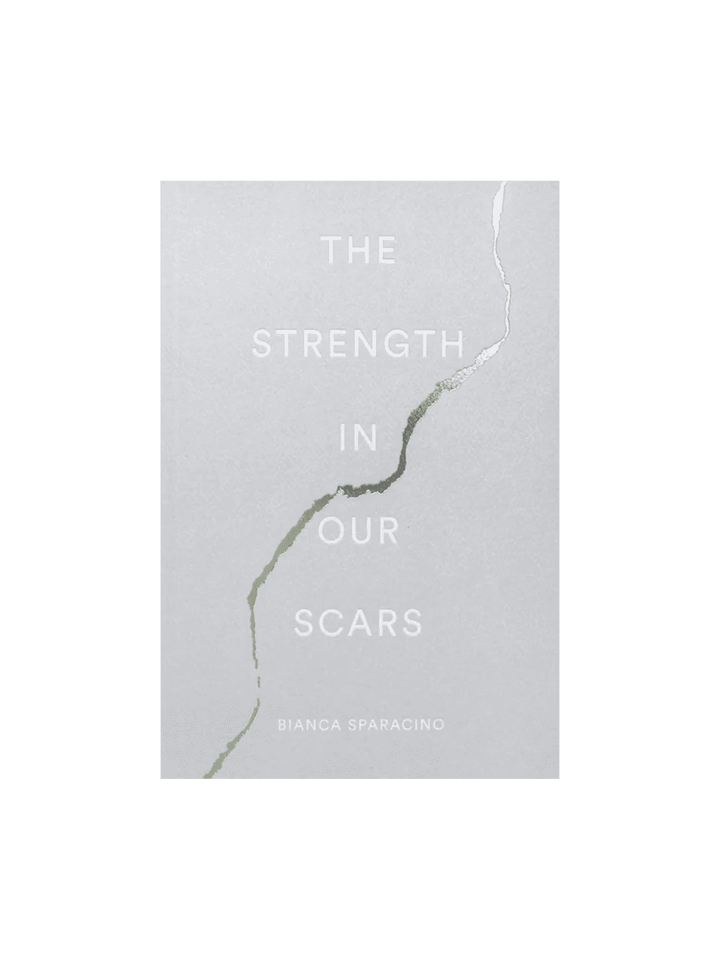 The front cover of The Strength In Our Scars by Bianca Sparacino features a light grey background with a stylized, kintsugi-inspired crack running down the middle | Twentyseven Toronto
