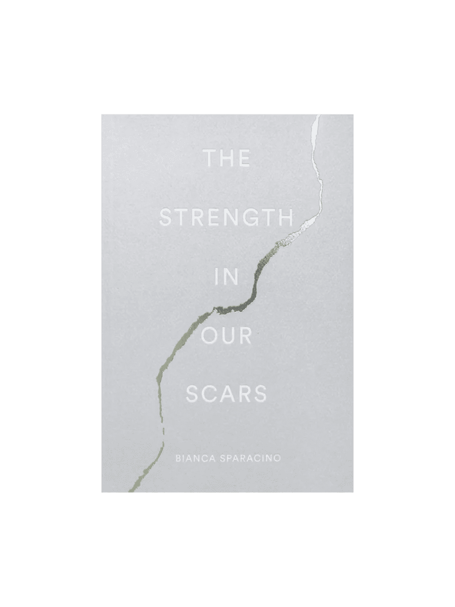 The front cover of The Strength In Our Scars by Bianca Sparacino features a light grey background with a stylized, kintsugi-inspired crack running down the middle | Twentyseven Toronto