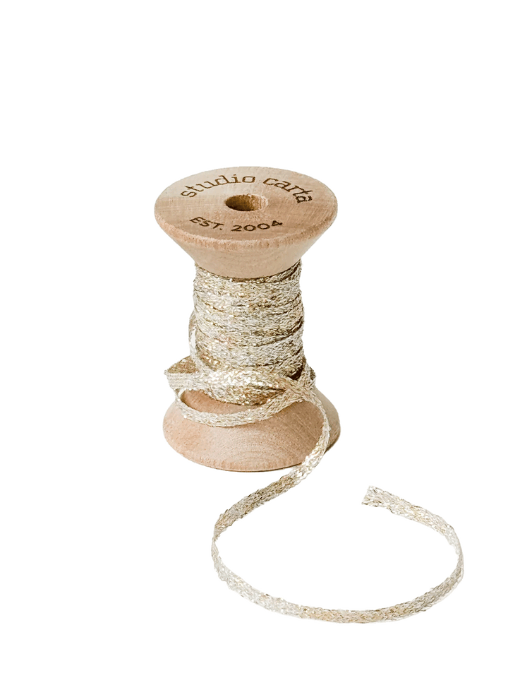 Studio Carta Metallic Braided Ribbon in Pearl wrapped around a wooden spool with ribbon unfurled | Twentyseven Toronto