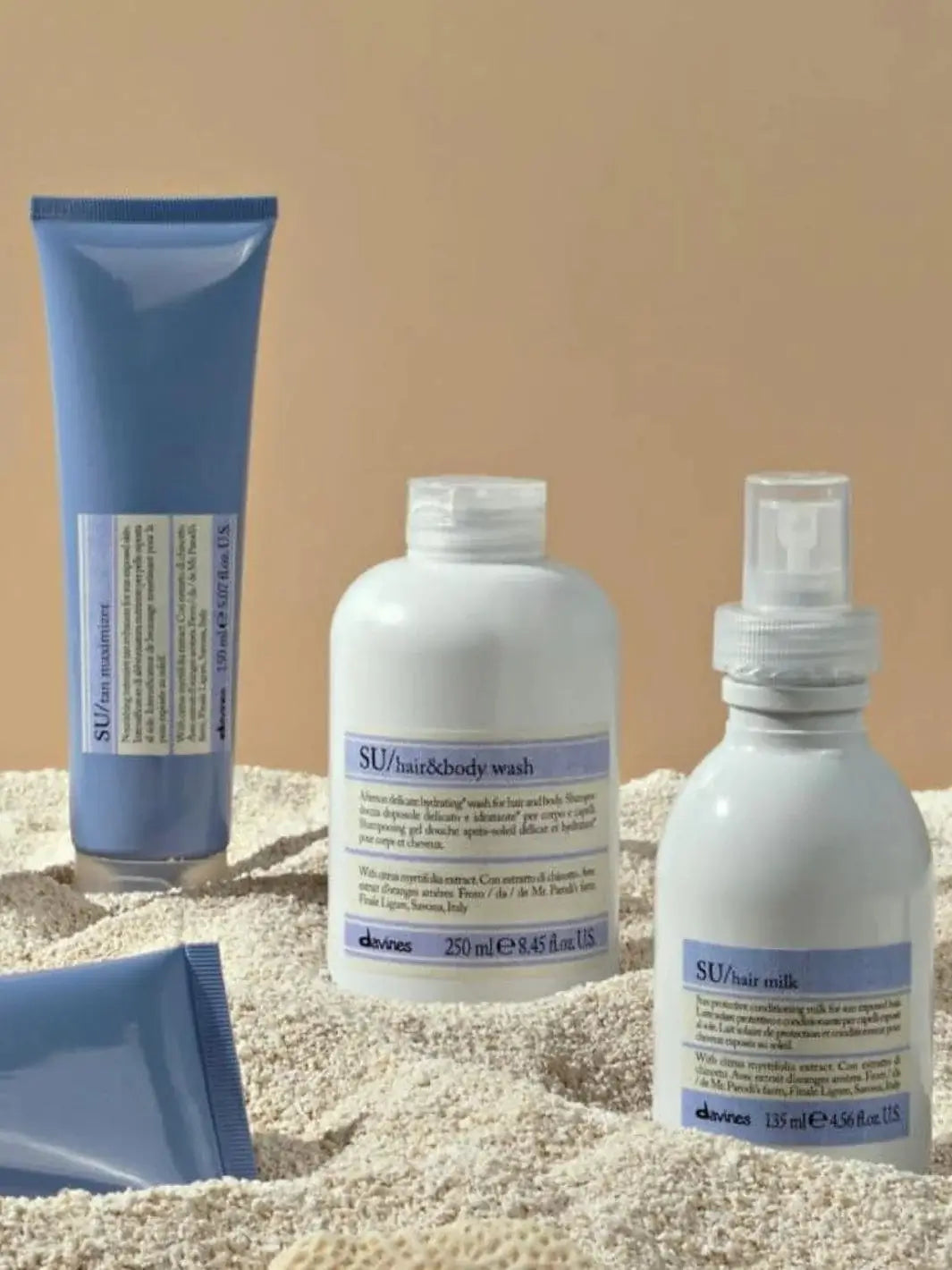 A bottle of Davines SU Hair and Body Wash stands in the sand alongside other sun care products from the Davines SU line | Twentyseven Toronto