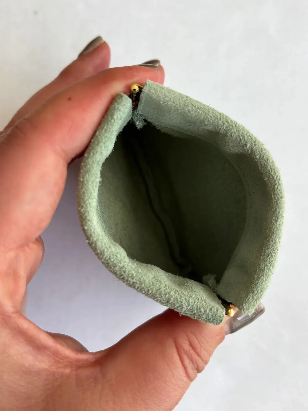 Hand holding a small sage green coin pouch against a white background | Twentyseven Toronto