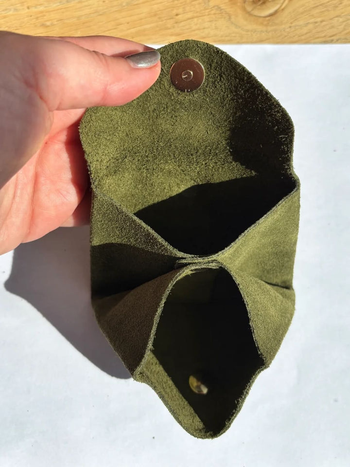 Deep green suede coin purse in 'Forest Green' with a gold button held by hand showing inside of coin purse | Twentyseven Toronto