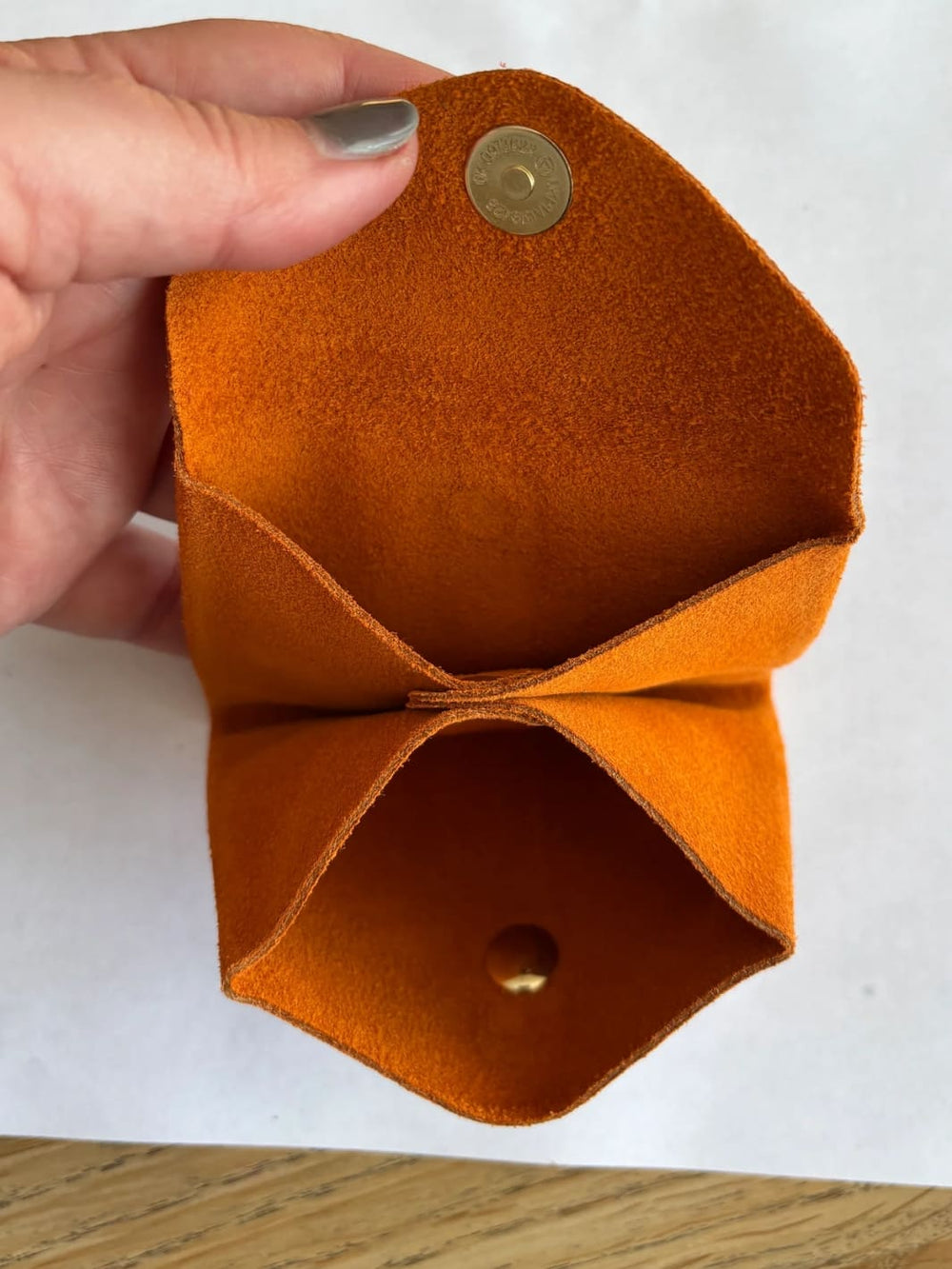 Orange suede coin purse with a gold button held by hand showing inside of coin purse | Twentyseven Toronto