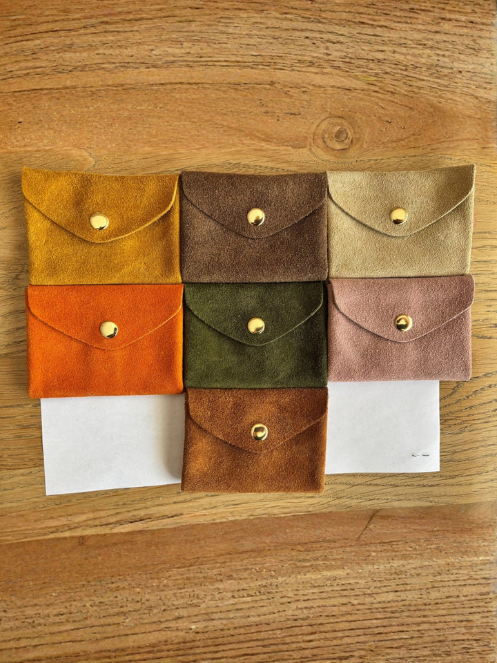 Set of seven suede coin pouches in various colours on a wooden surface | Twentyseven Toronto