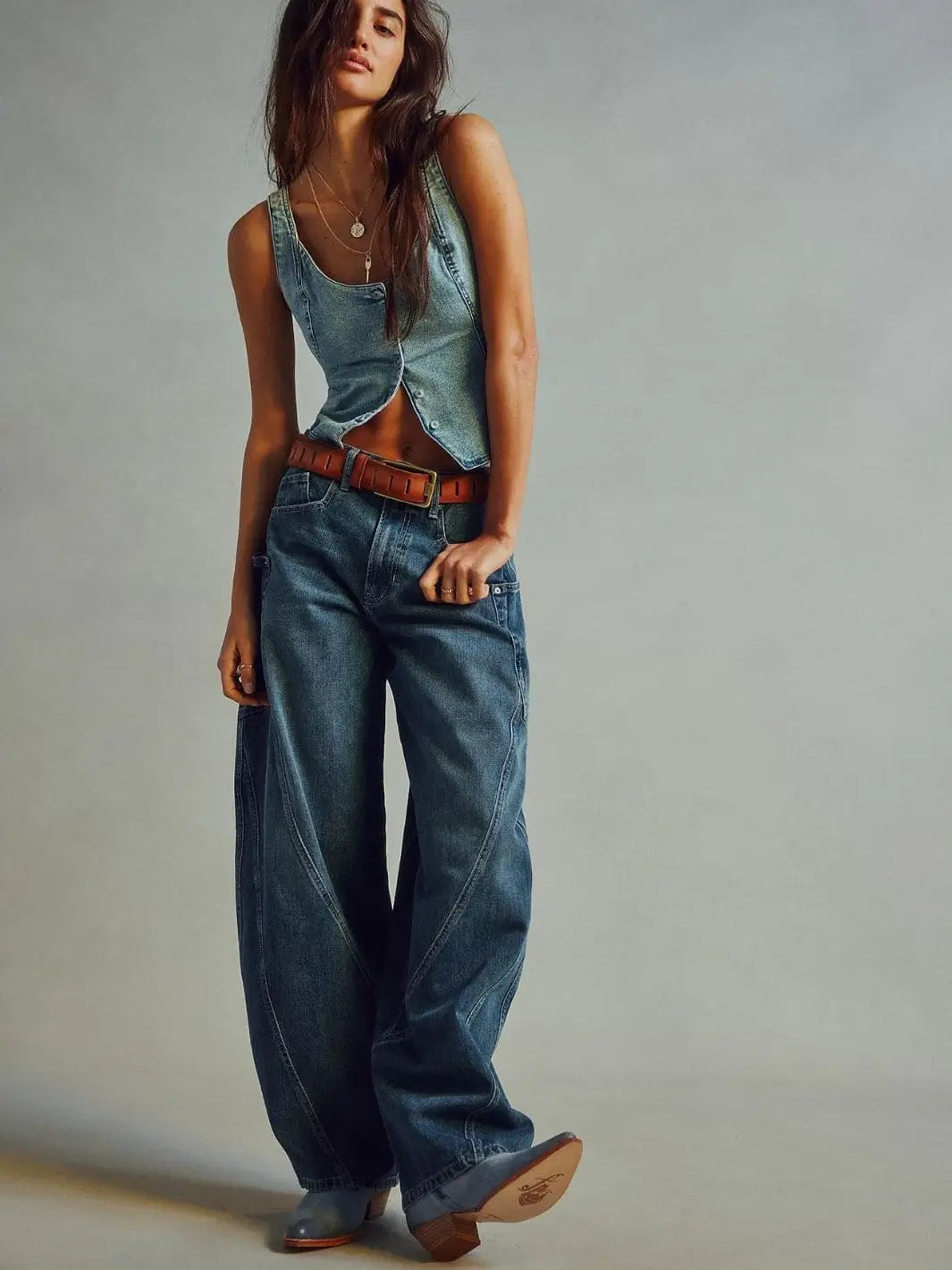 A model poses in the wide-leg Free People Sugar And Spice Barrel Jeans - Beatrix Indigo styled with a matching denim vest, a brown belt, and boots | Twentyseven Toronto