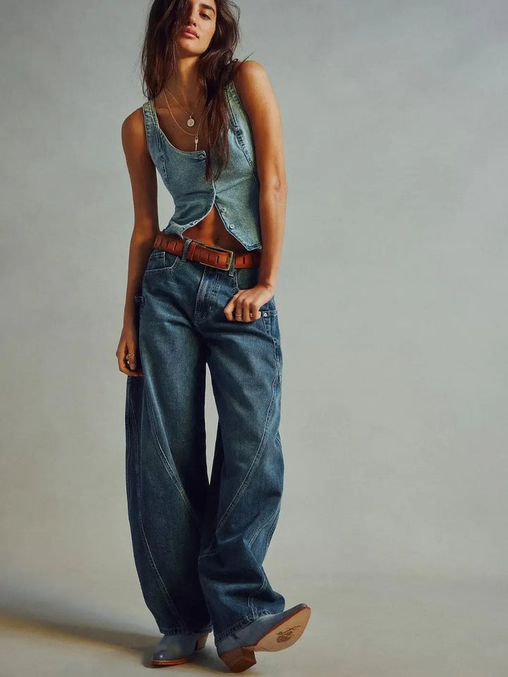 A model poses in the wide-leg Free People Sugar And Spice Barrel Jeans - Beatrix Indigo styled with a matching denim vest, a brown belt, and boots | Twentyseven Toronto