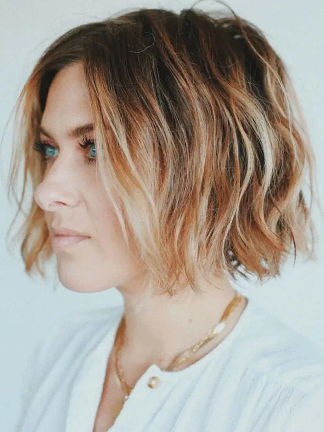 A profile view of a model with a textured, wavy blonde bob styled with R+Co SUN CATCHER Leave in Conditioner | Twentyseven Toronto