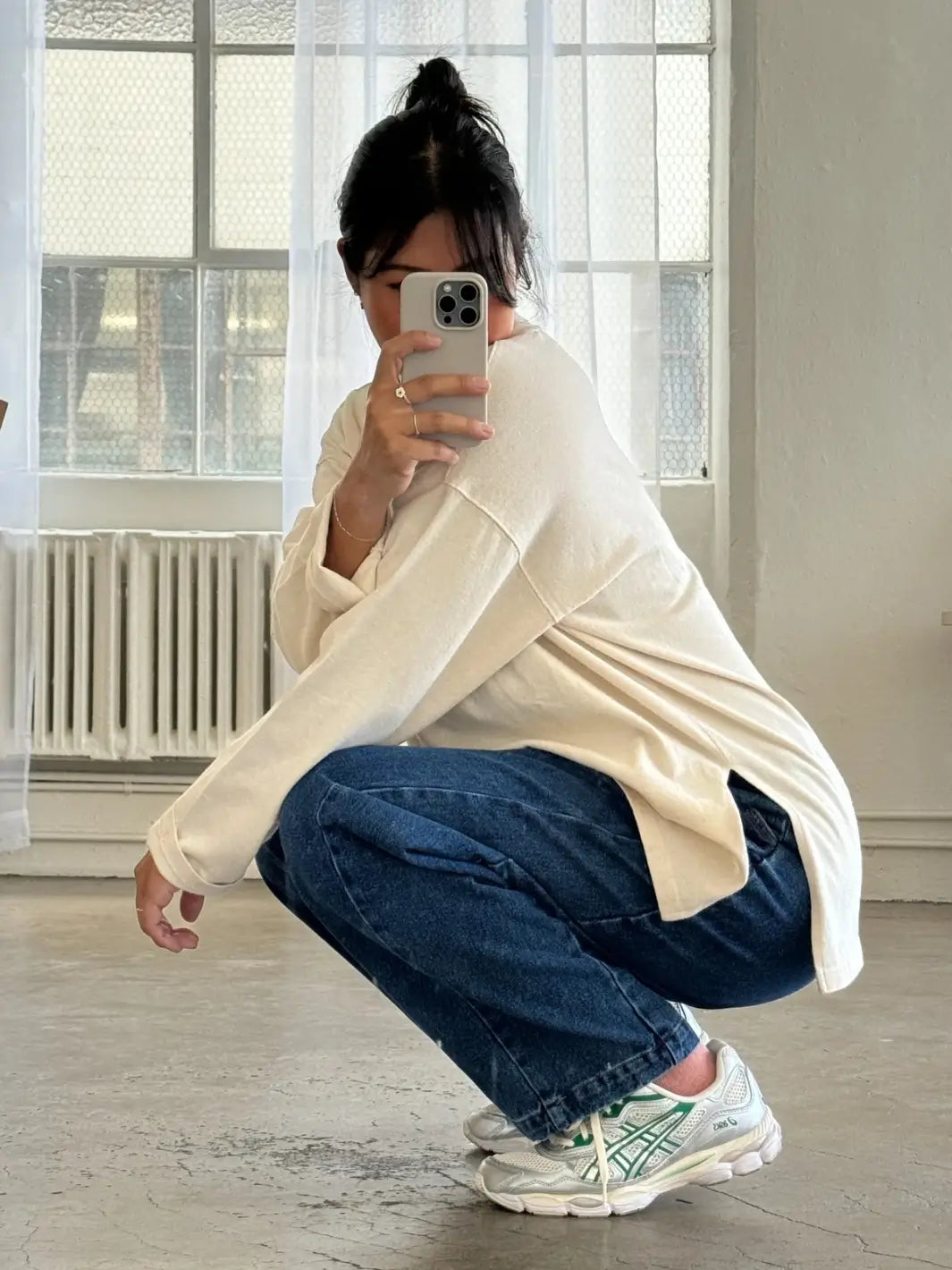 Person wearing a beige 'Sunday Tee' sweater in 'Naturel' and blue jeans from Le Bon Shoppe, squatting in a room with large windows | Twentyseven Toronto