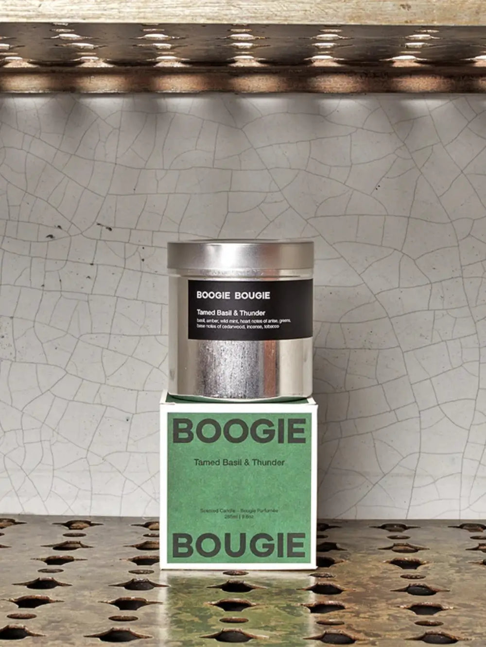 Silver Tamed Basil and Thunder candle container from Boogie and Bougie green product packaging on a textured surface with a cracked wall background | Twentyseven Toronto