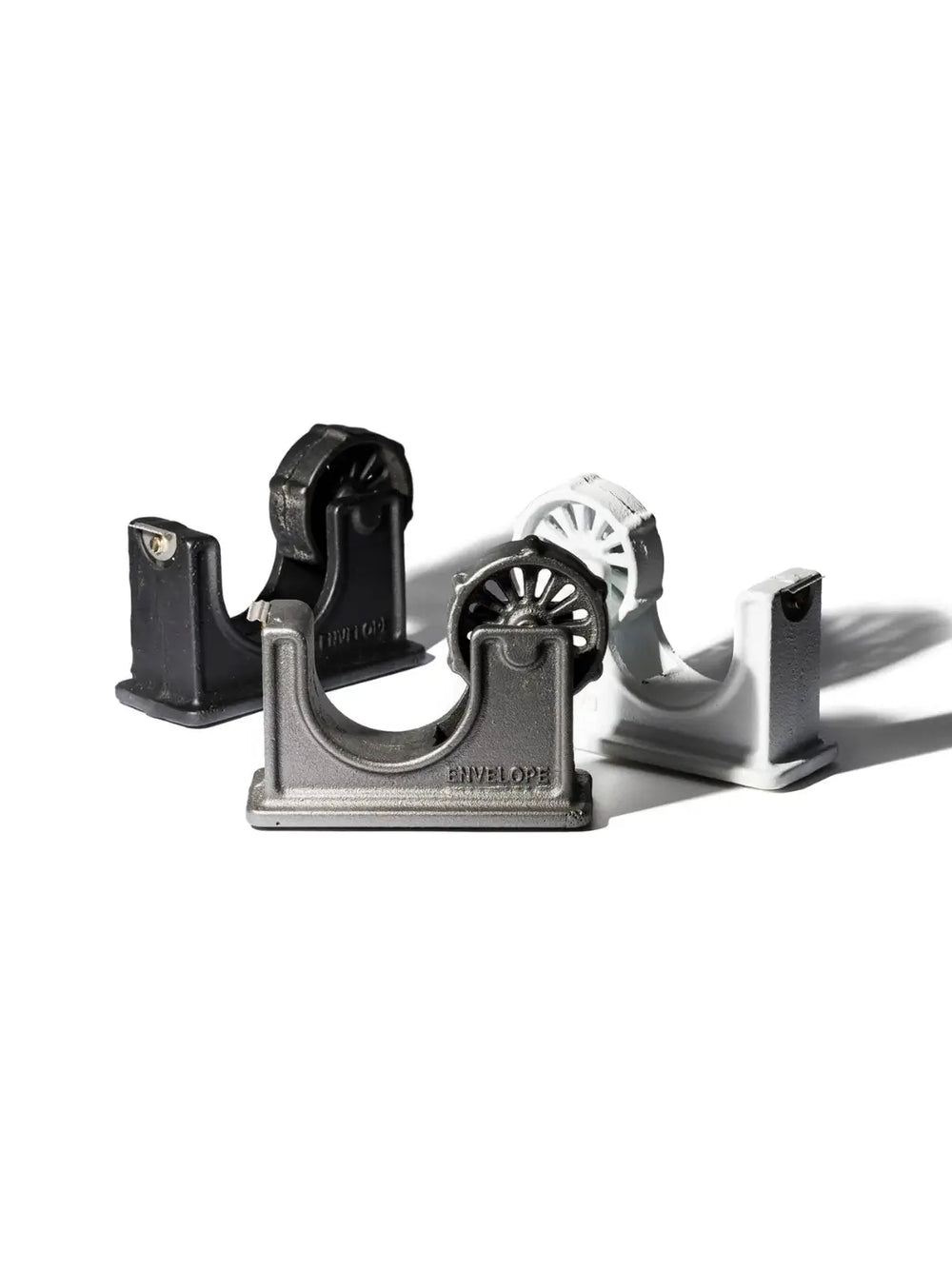 A collection of three heavy iron office organizers including the grey Tape Dispenser - Natural from Puebco in the foreground with "ENVELOPE" embossed on its side | Twentyseven Toronto