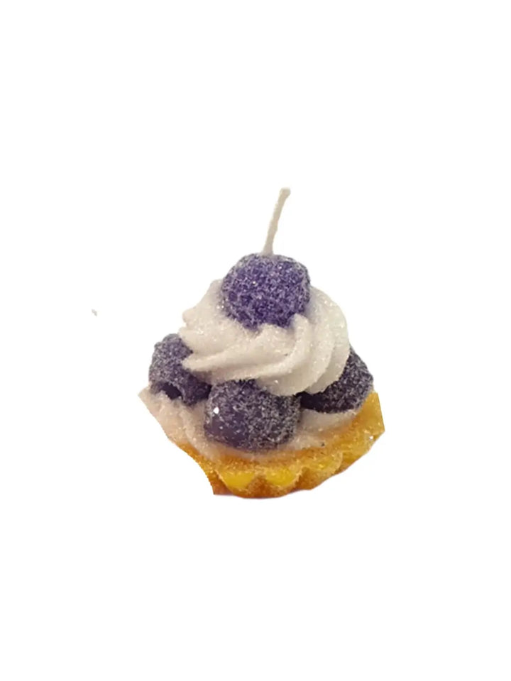 Candle shaped like a tart with white frosting and purple berries from Cereria Introna on a white background | Twentyseven Toronto