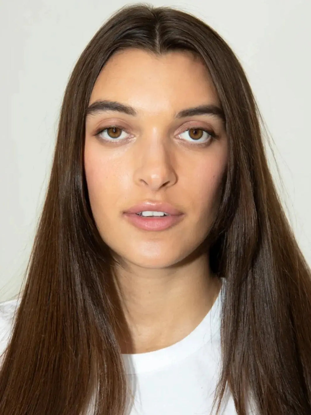 A close-up portrait of a model showcasing long, sleek, and healthy brunette hair styled with R+Co TELEVISION Perfect Hair Masque | Twentyseven Toronto