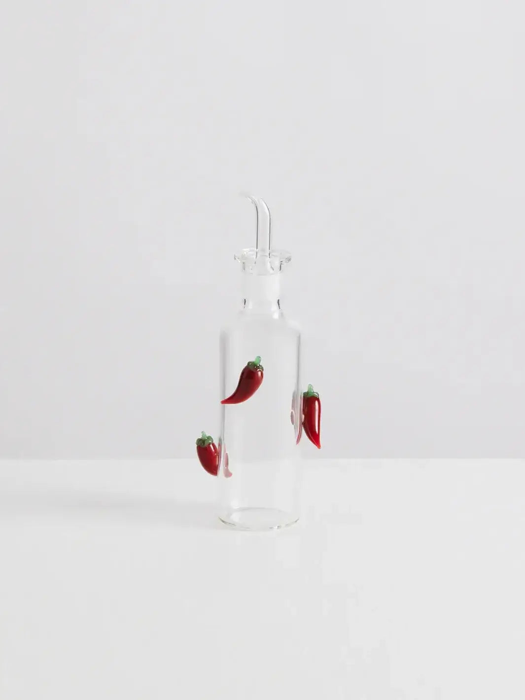 Clear glass bottle with decorative red chili peppers from Maison Balzac on a white background | Twentyseven Toronto