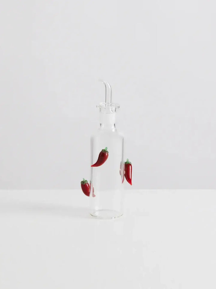 Clear glass bottle with decorative red chili peppers from Maison Balzac on a white background | Twentyseven Toronto