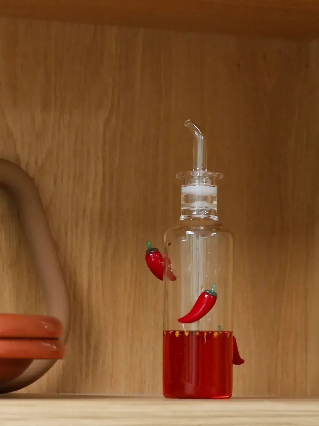 Clear glass bottlewith decorative red chili peppers from Maison Balzac on a wooden surface | Twentyseven Toronto