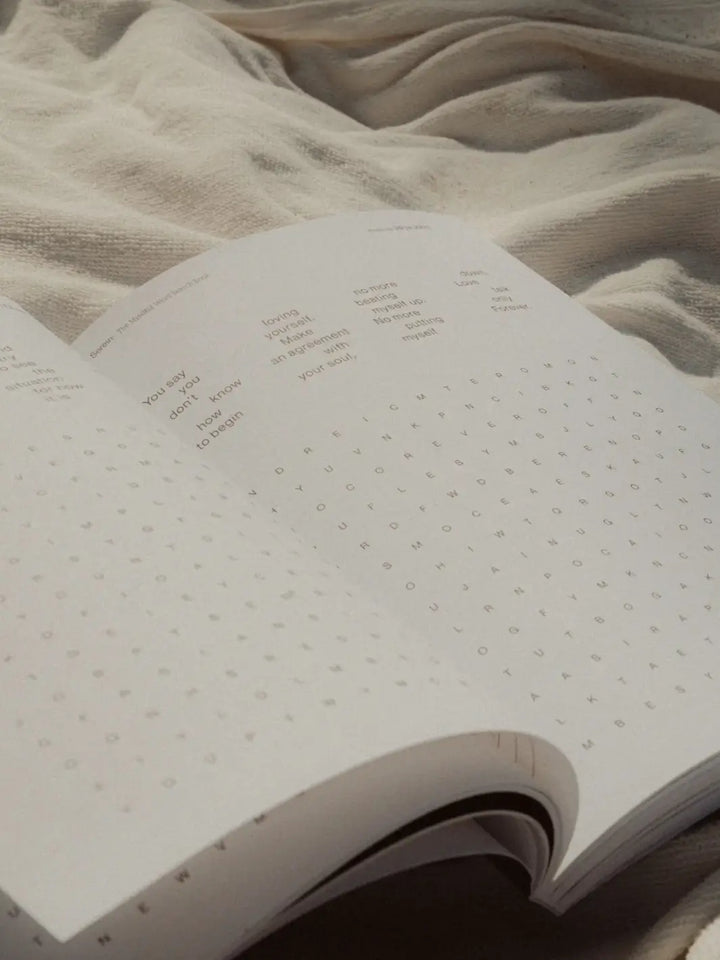 An open copy of Serein The Mindful Word Search Book rests flat on a textured cream-colored blanket, displaying clean typography and grid layouts | Twentyseven Toronto