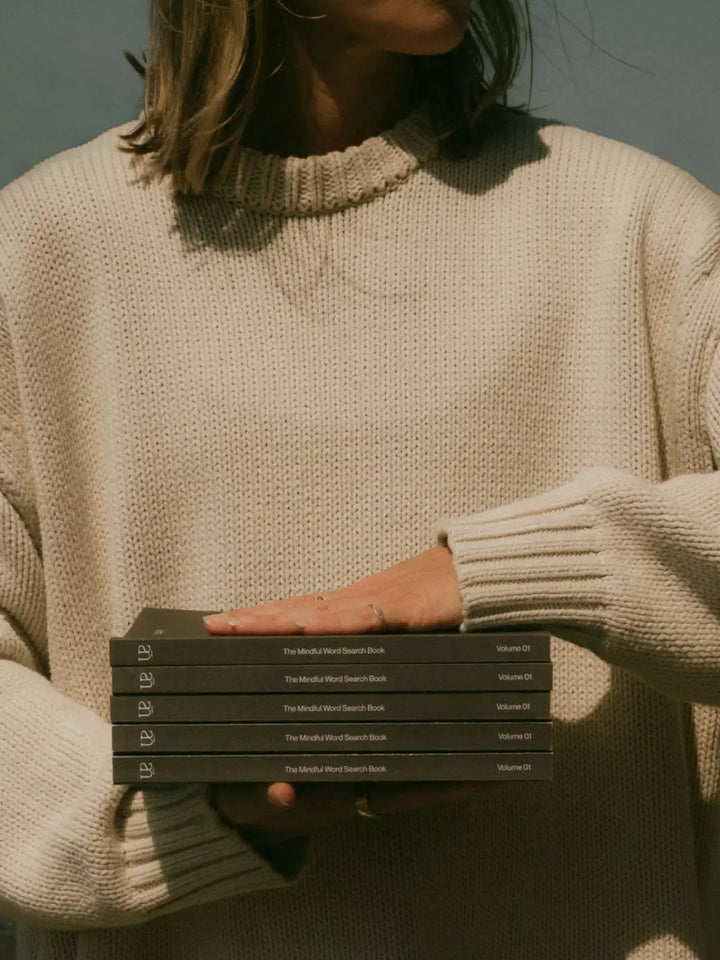 A person dressed in a chunky cream knit sweater holds a stack of five copies of Serein The Mindful Word Search Book Volume 01 | Twentyseven Toronto