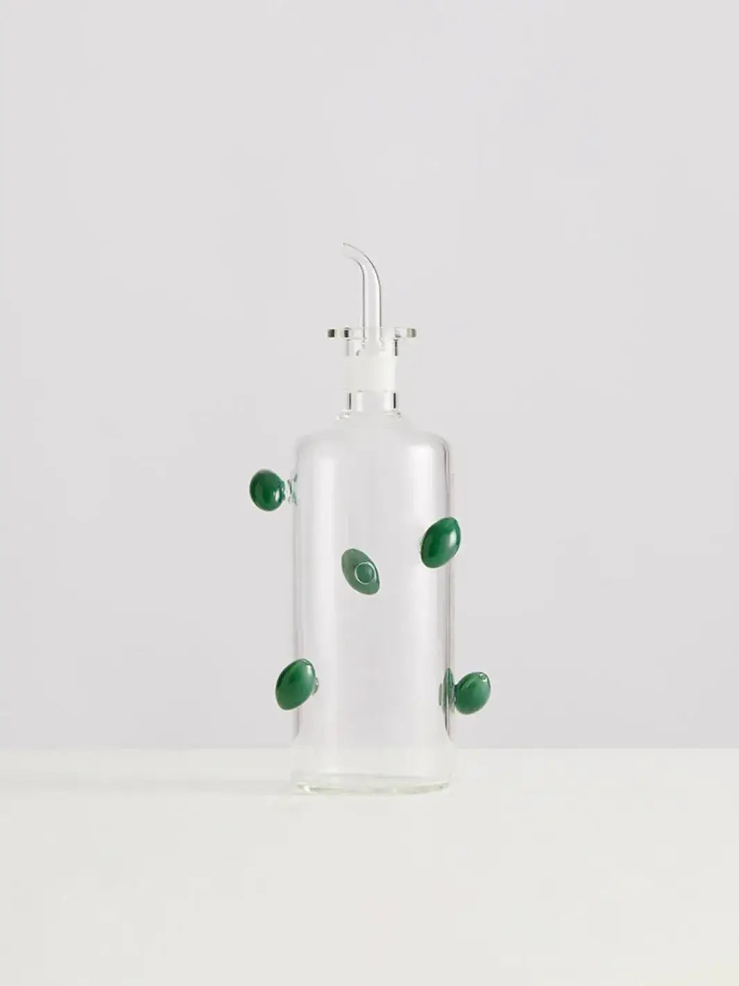 Glass olive dispenser bottle from Maison Balzac decorated with green olives on a white background | Twentyseven Toronto
