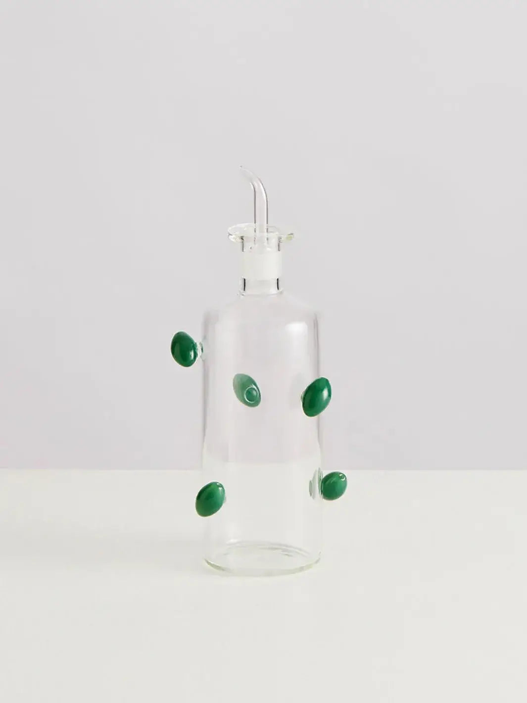 Glass olive dispenser bottle from Maison Balzac decorated with green olives on a white background | Twentyseven Toronto
