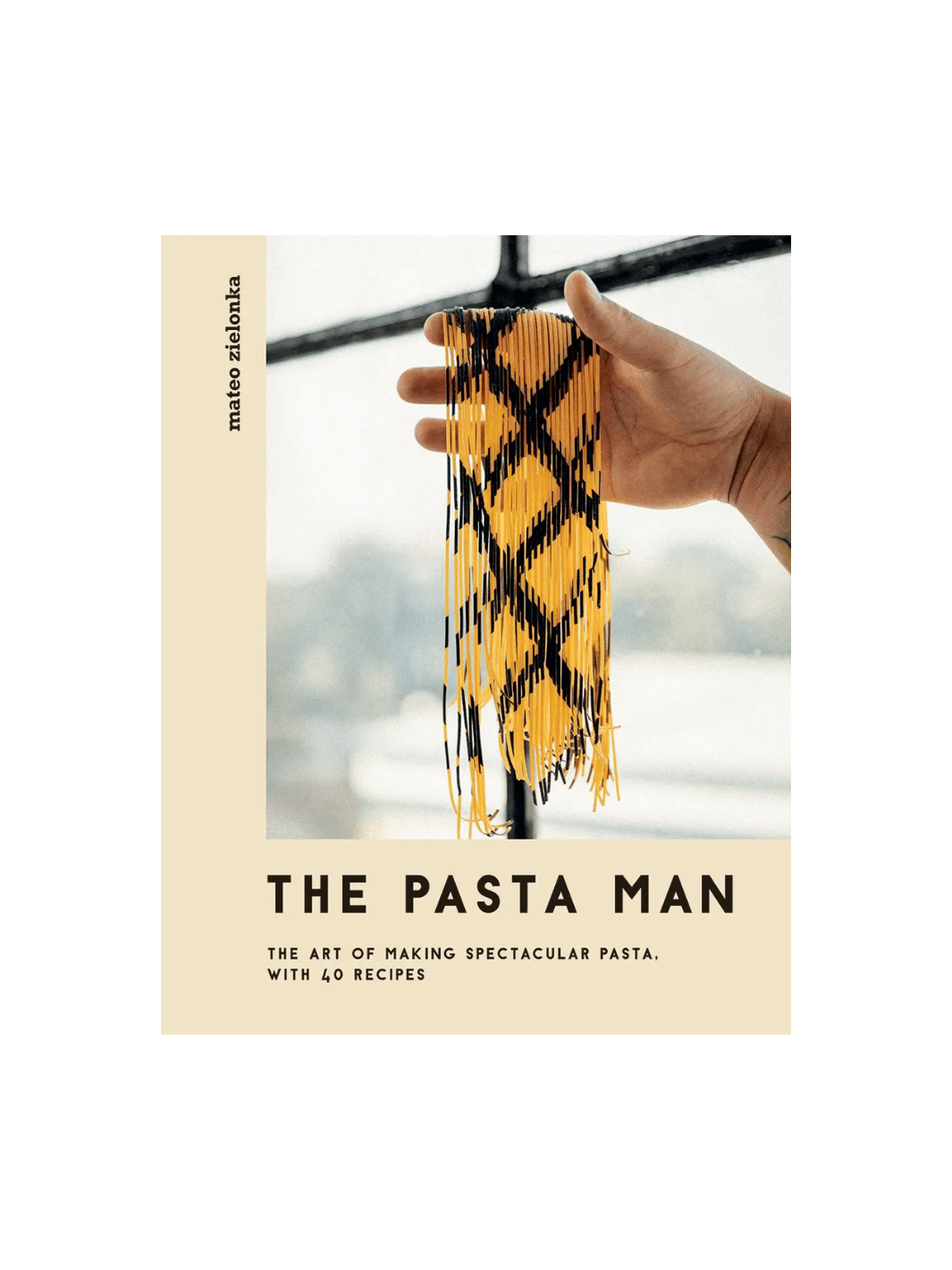 Front cover of The Pasta Man: The Art of Making Spectacular Pasta by Mateo Zielonka features a hand holding up long strands of intricately patterned yellow and black pasta against a bright window | Twentyseven Toronto