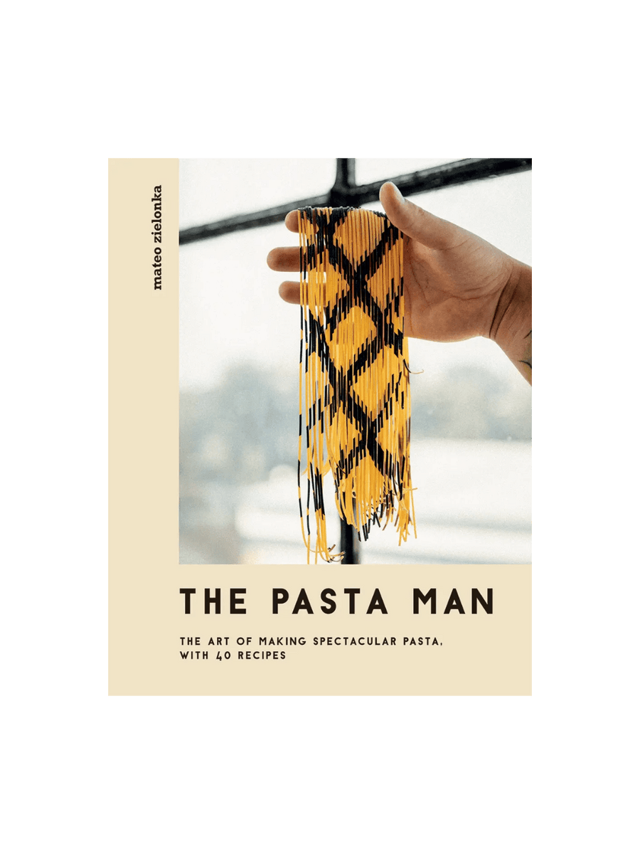 Front cover of The Pasta Man: The Art of Making Spectacular Pasta by Mateo Zielonka features a hand holding up long strands of intricately patterned yellow and black pasta against a bright window | Twentyseven Toronto