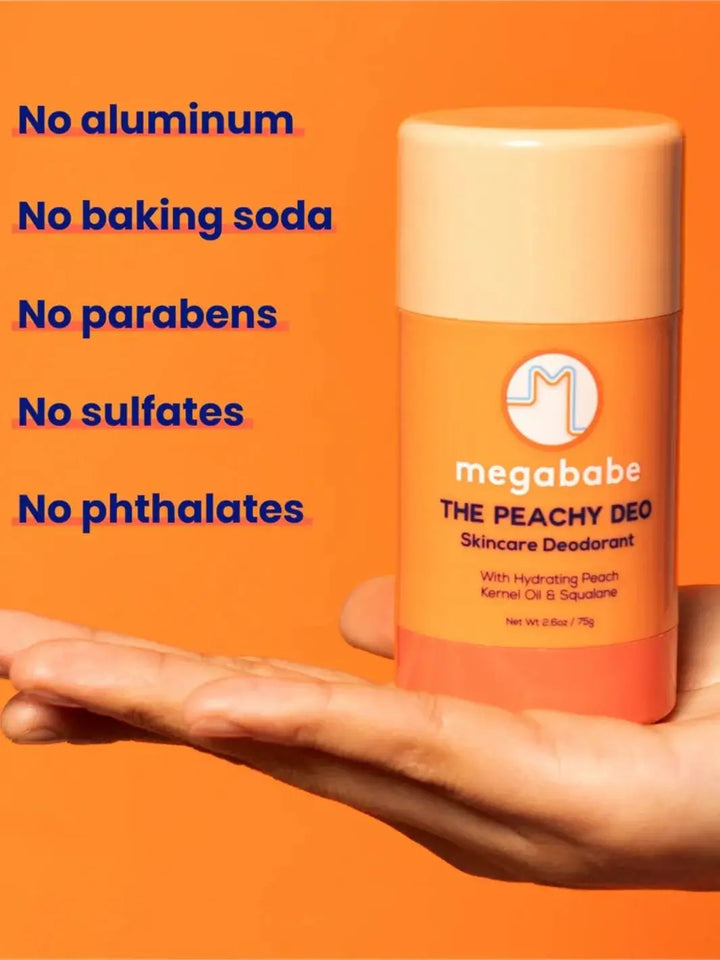 A hand supports a stick of Megababe The Peachy Deo in their palm against a bright orange background showcasing its clean ingredient benefits | Twentyseven Toronto