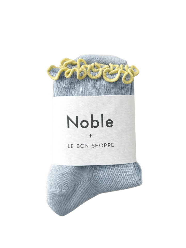 A pair of Petite Ruffled Modal Socks in Baby Blue / Butter from Le Bon Shoppe is displayed with its white "Noble + LE BON SHOPPE" collaborative packaging band | Twentyseven Toronto