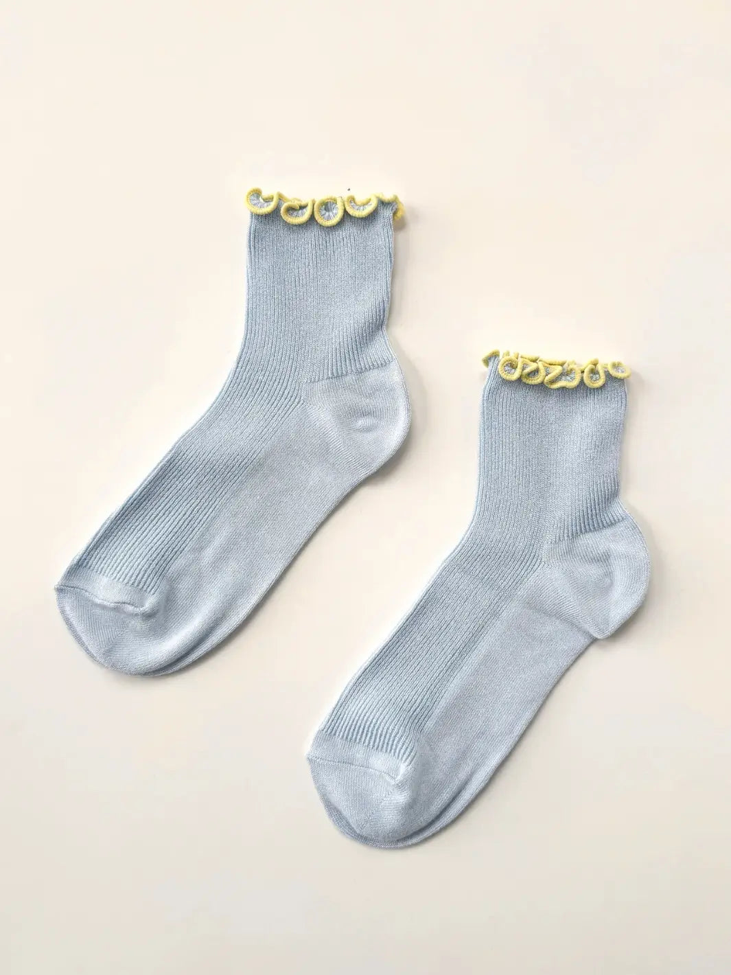 A flat-lay view captures a of pair baby blue and yellow Petite Ruffled Modal Socks in Baby Blue / Butter from Le Bon Shoppe resting on a white background | Twentyseven Toronto