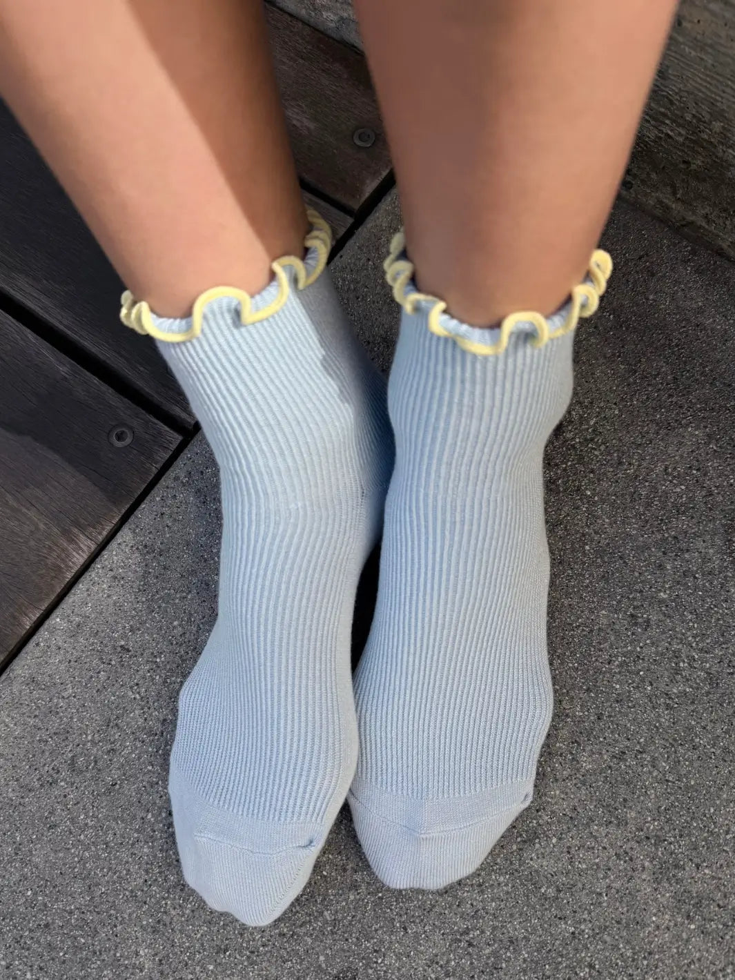 A top-down view shows The Petite Ruffled Modal Socks in Baby Blue / Butter from Le Bon Shoppe being worn against a concrete floor | Twentyseven Toronto